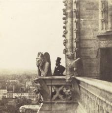 Photographie en noir et blanc d'un statue des tours de Notre Dame de Paris avec un homme en haut de forme