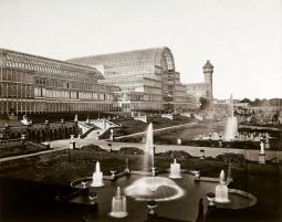 Photographie en noir et blanc d'une architecture en verre et fer, jardins avec des jets d'eau