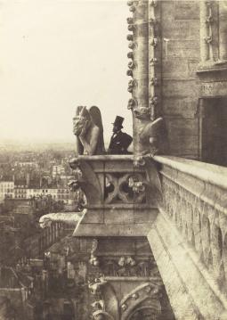 Photographie en noir et blanc d'un statue des tours de Notre Dame de Paris avec un homme en haut de forme