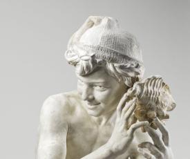 jeune garçon accroupi coiffé d'un bonnet écoutant une coquille