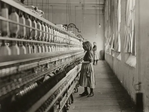 Photo noir et blanc d'une jeune fille travaillant seule dans une filature textile, alignée devant de longues rangées de bobines de fil