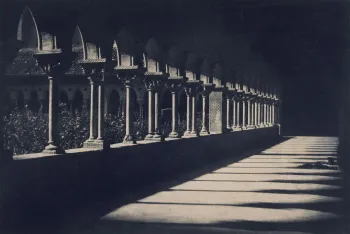 Photographie noir et blanc d'une galerie de cloître aux colonnades gothiques, jouant sur les jeux d'ombre et de lumière projetés au sol.